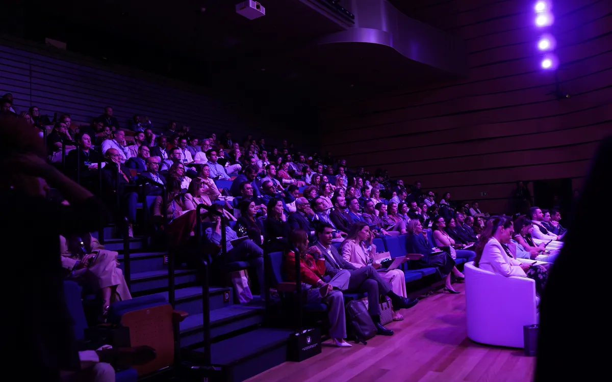 Plateia completa durante a aula principal, em iluminação roxa